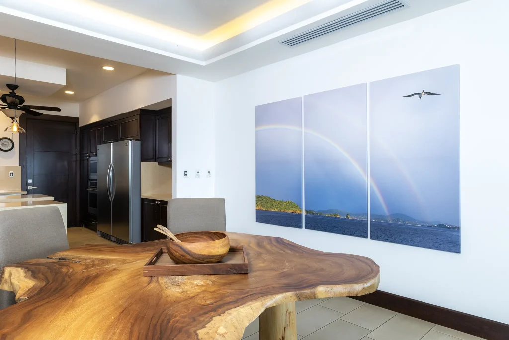 360 Splendor dining area with a live-edge wood table and ocean-photo triptych beside an open kitchen
