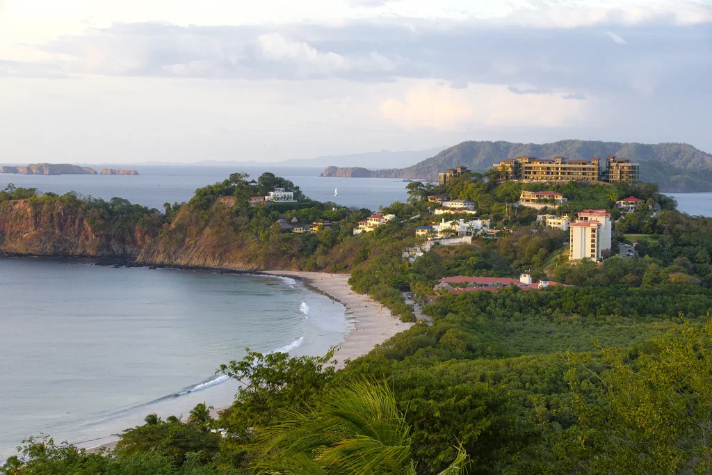 Aerial view of Flamingo Beach, Costa Rica, with the 360 Splendor residences on the forested ridge above a white-sand cove