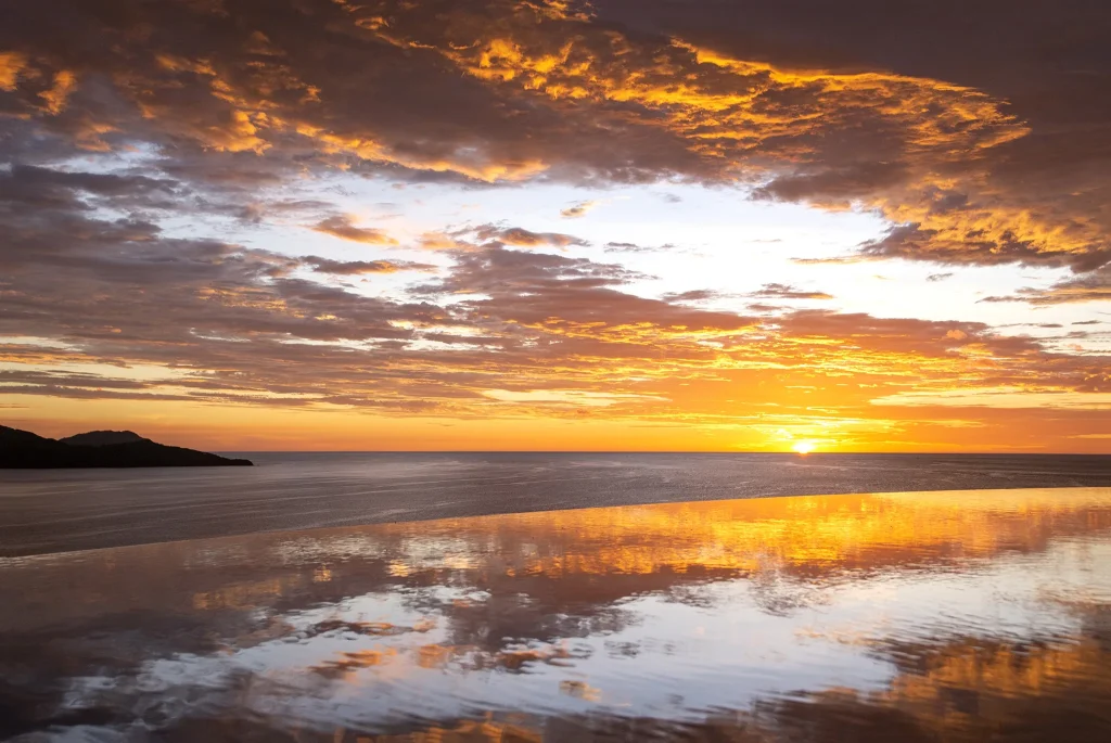 Golden sunset over the ocean reflected in the infinity pool's edge at 360 Splendor, with the headland of Flamingo Beach to the left.