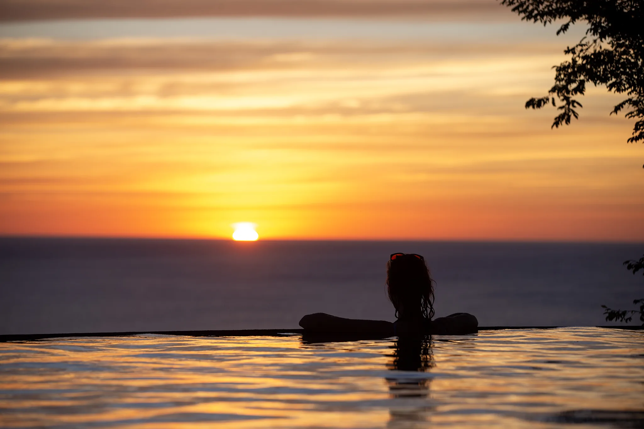 A guest relaxing at the infinity pool's edge at 360 Splendor as the sun sets over the ocean